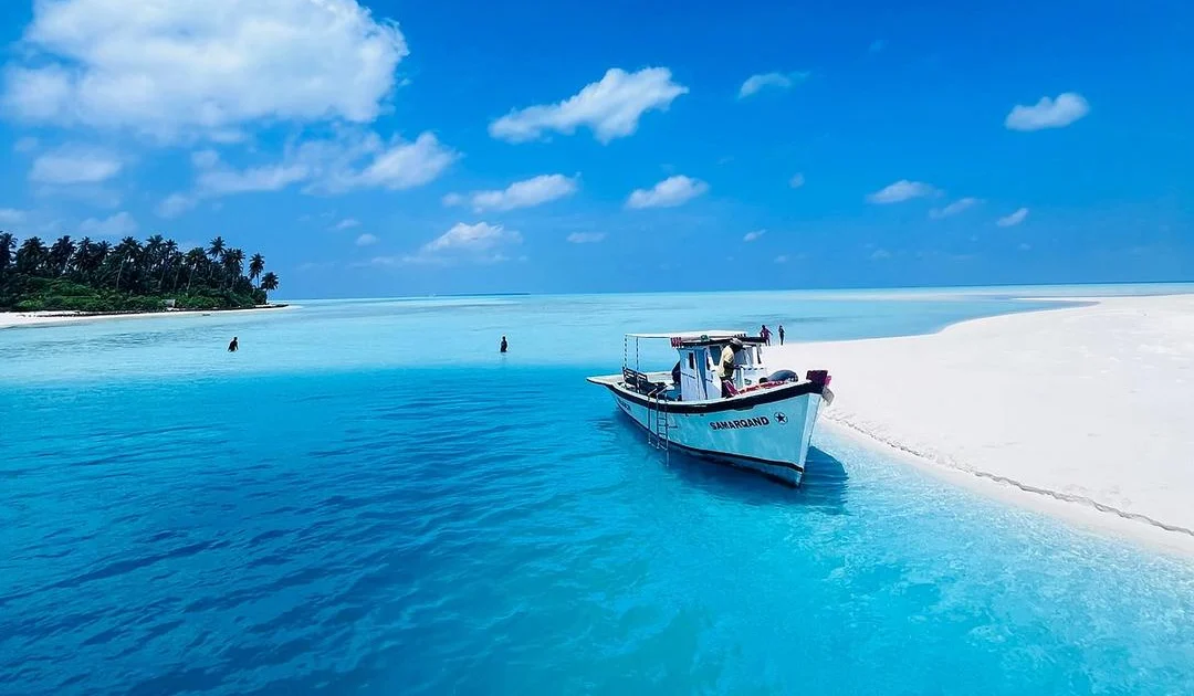 A small island boat beside a white sandbank in clear turquoise water