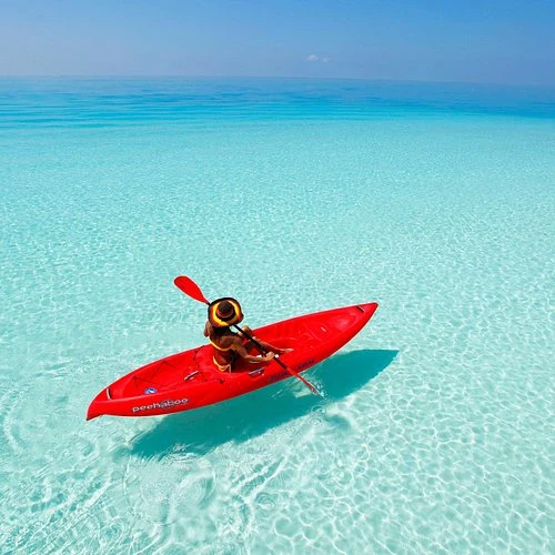 A paddler in a red kayak on clear turquoise lagoon water